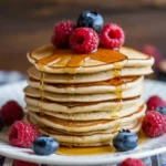 A stack of fluffy vegan pancakes topped with syrup and fresh berries.